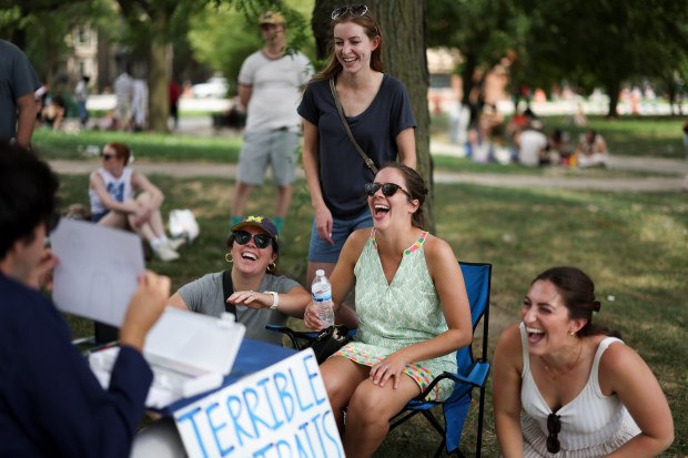 Friends Abbey Londa, from left, Becca Weisz, Lauren Smith, and Francesca Sands laugh as they look at the portrait Jacob Ryan Reno drew of them in Logan Square Park on Sunday, Aug. 10, 2025. Reno draws "terrible" portraits of people for $5. (Eileen T. Meslar/Chicago Tribune)