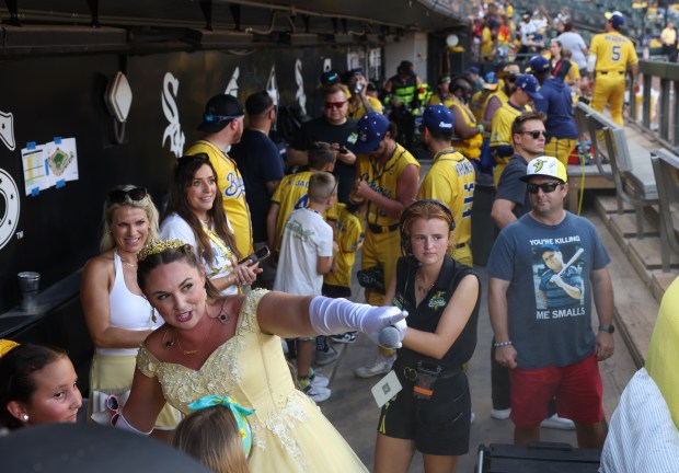 A Savannah Bananas cast member stage-named Princess Potassia points out details to young fans in the dugout before a game against the Firefighters on Aug. 15, 2025, at Rate Field. (John J. Kim/Chicago Tribune)