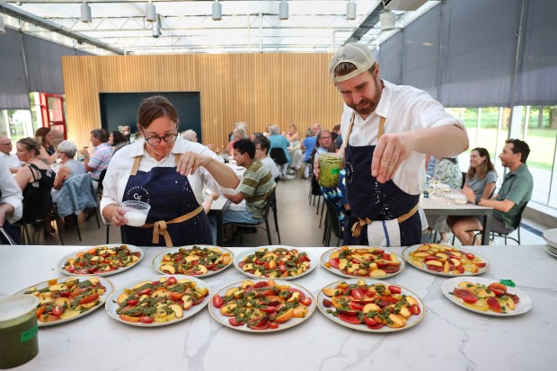 General manager Anna Rafalski and sous chef Jason Garland, right, add coarse salt to family style platters of the season's first tomatoes with peaches and kale pesto during a Summer Supper in a greenhouse at Granor Farm in Three Oaks, Michigan on Aug. 7, 2025. (Chris Sweda/Chicago Tribune)