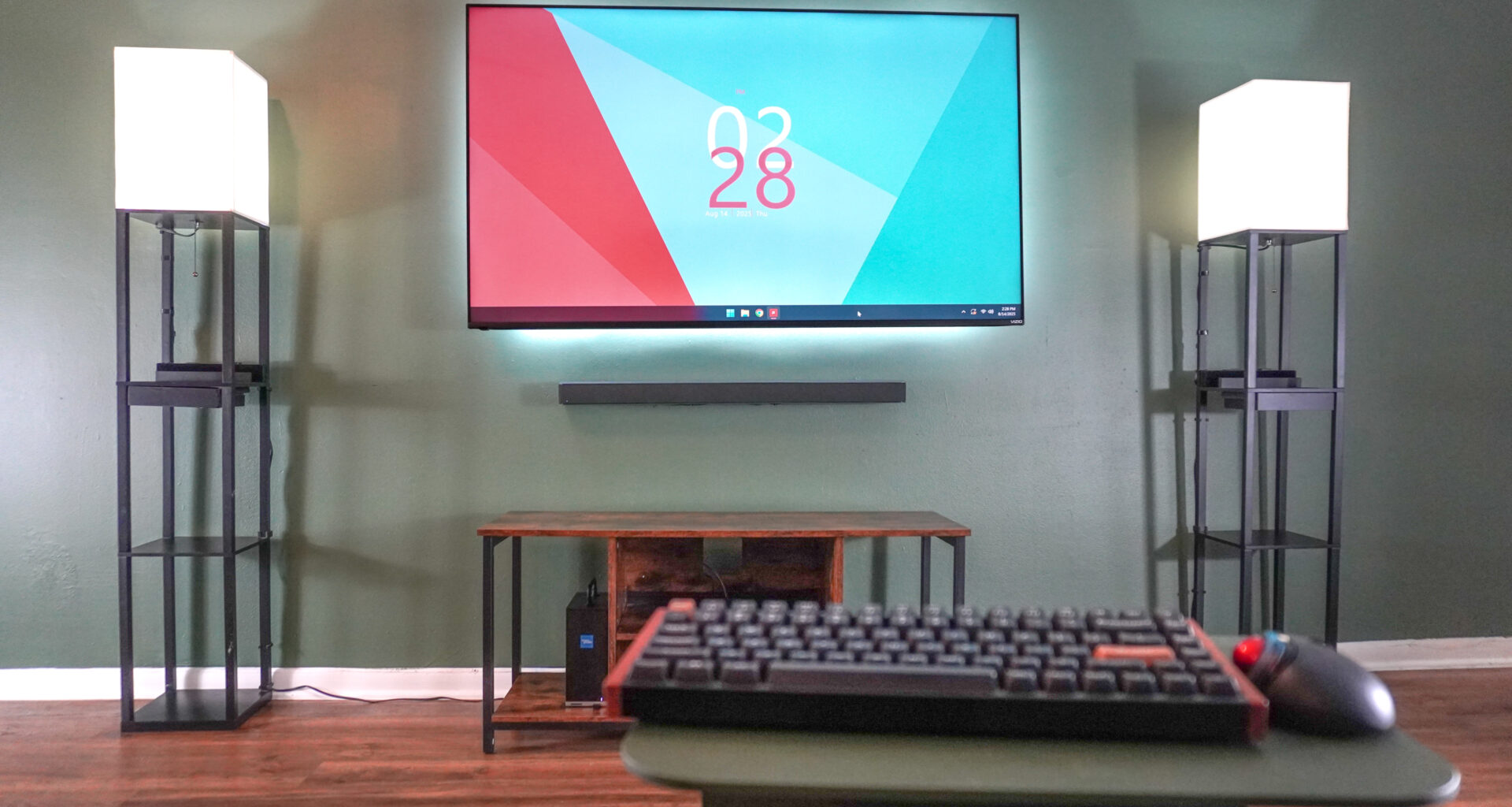 A mouse and keyboard in front of a TV with the Framework Desktop in the left corner of an entertainment center
