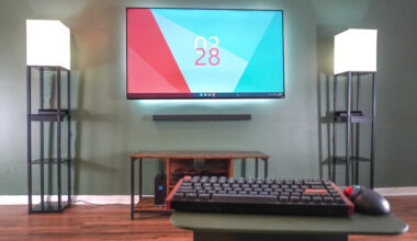 A mouse and keyboard in front of a TV with the Framework Desktop in the left corner of an entertainment center