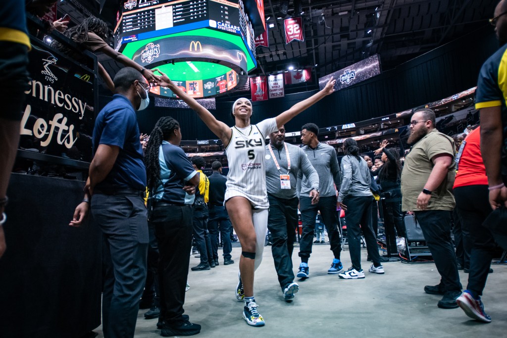 Chicago Sky forward Angel Reese smiles and raises arms towards fans on the court after a game