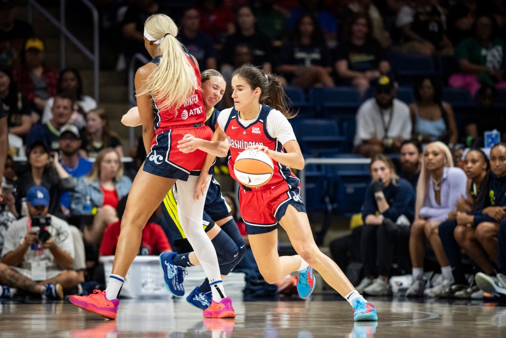 Washington Mystics forward Kiki Iriafen sets a screen on Dallas Wings guard Paige Bueckers a few steps inside the 3-point line. Mystics guard Sonia Citron dribbles the ball with her left hand around Iriafen's screen.