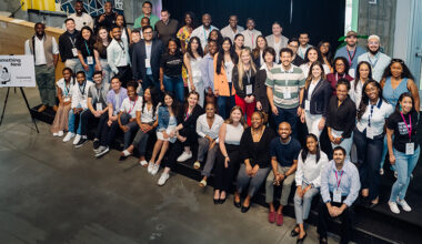 A large group of people some sitting and some standing on a stage pose for a photo.