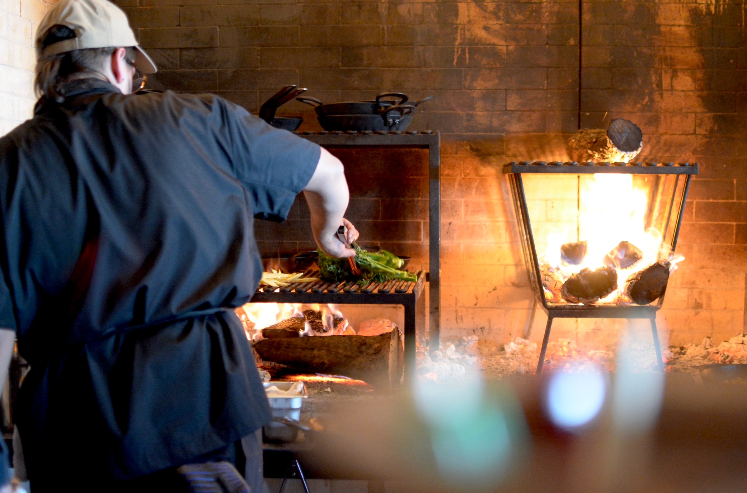 Chef cooking broccolini over the fire hearth at Betsy