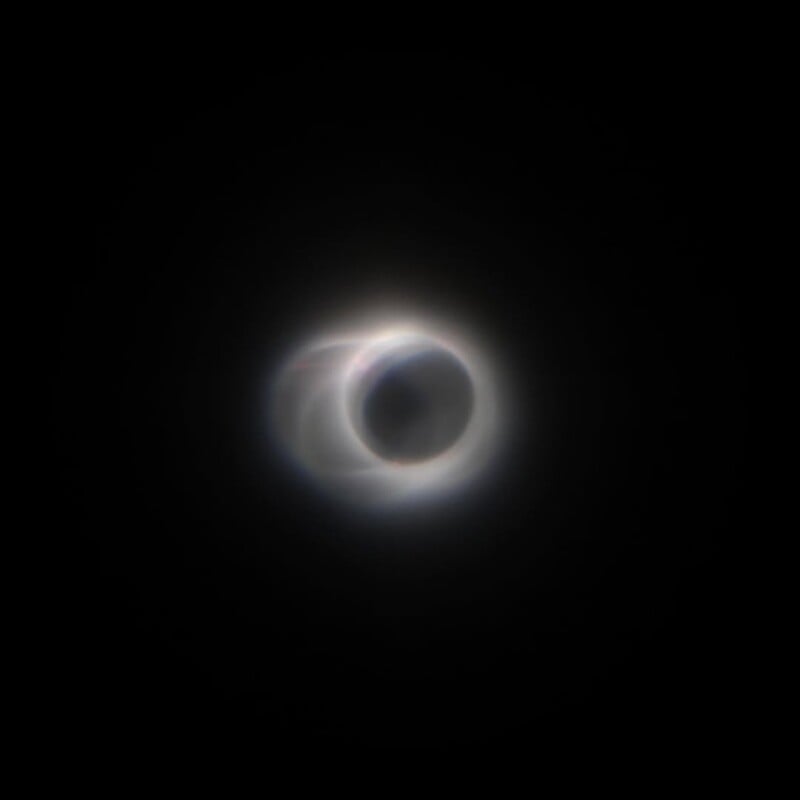 A total solar eclipse with the Moon completely covering the Sun, creating a glowing corona of light around a dark central circle against a black sky.