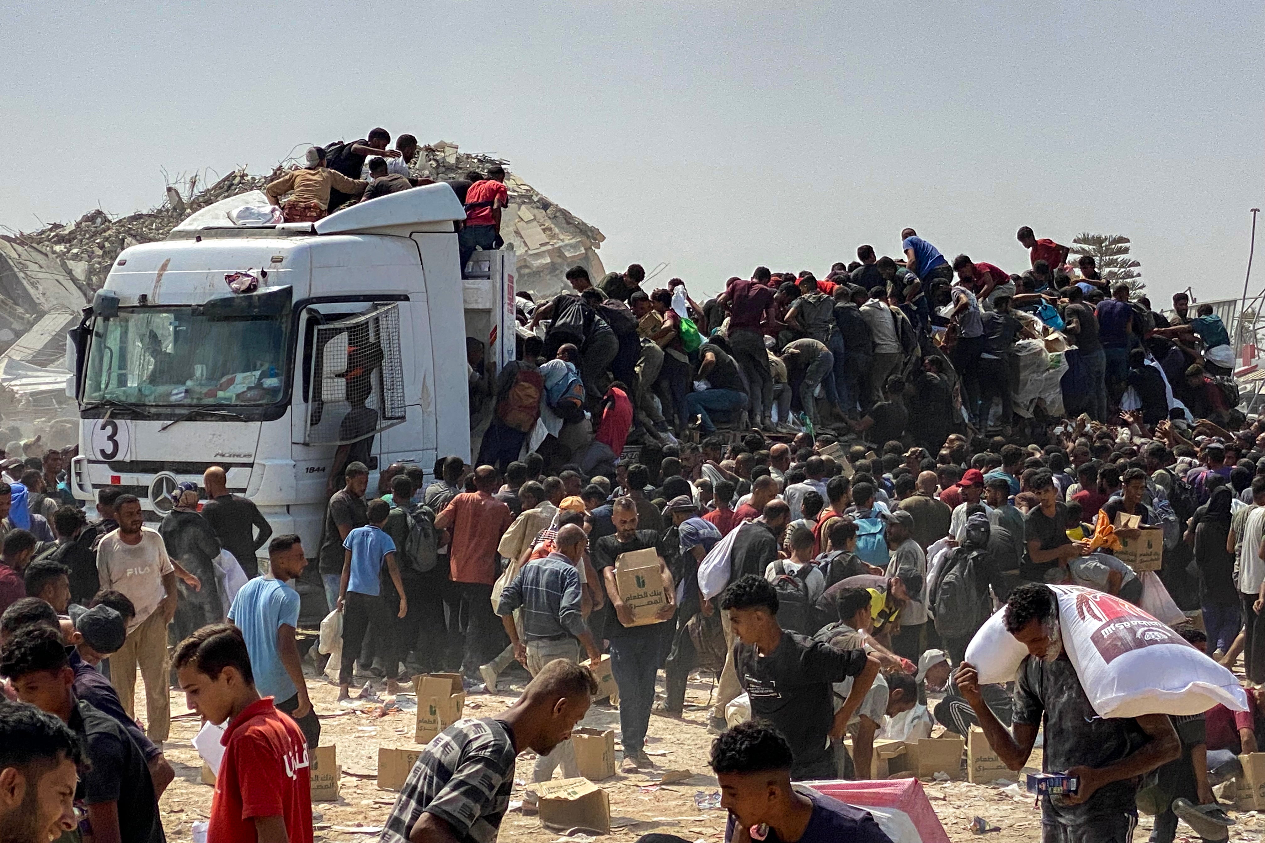 Displaced Palestinians carry food parcels as they raid trucks carrying humanitarian aid in Khan Yunis, in the southern Gaza Strip on August 9, 2025.