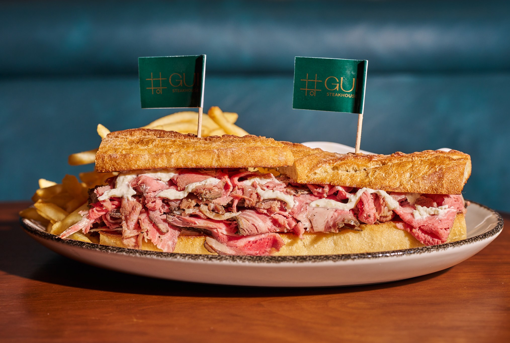 A long sandwich with slices of meat and two toothpicks with green tabs reading Gui.