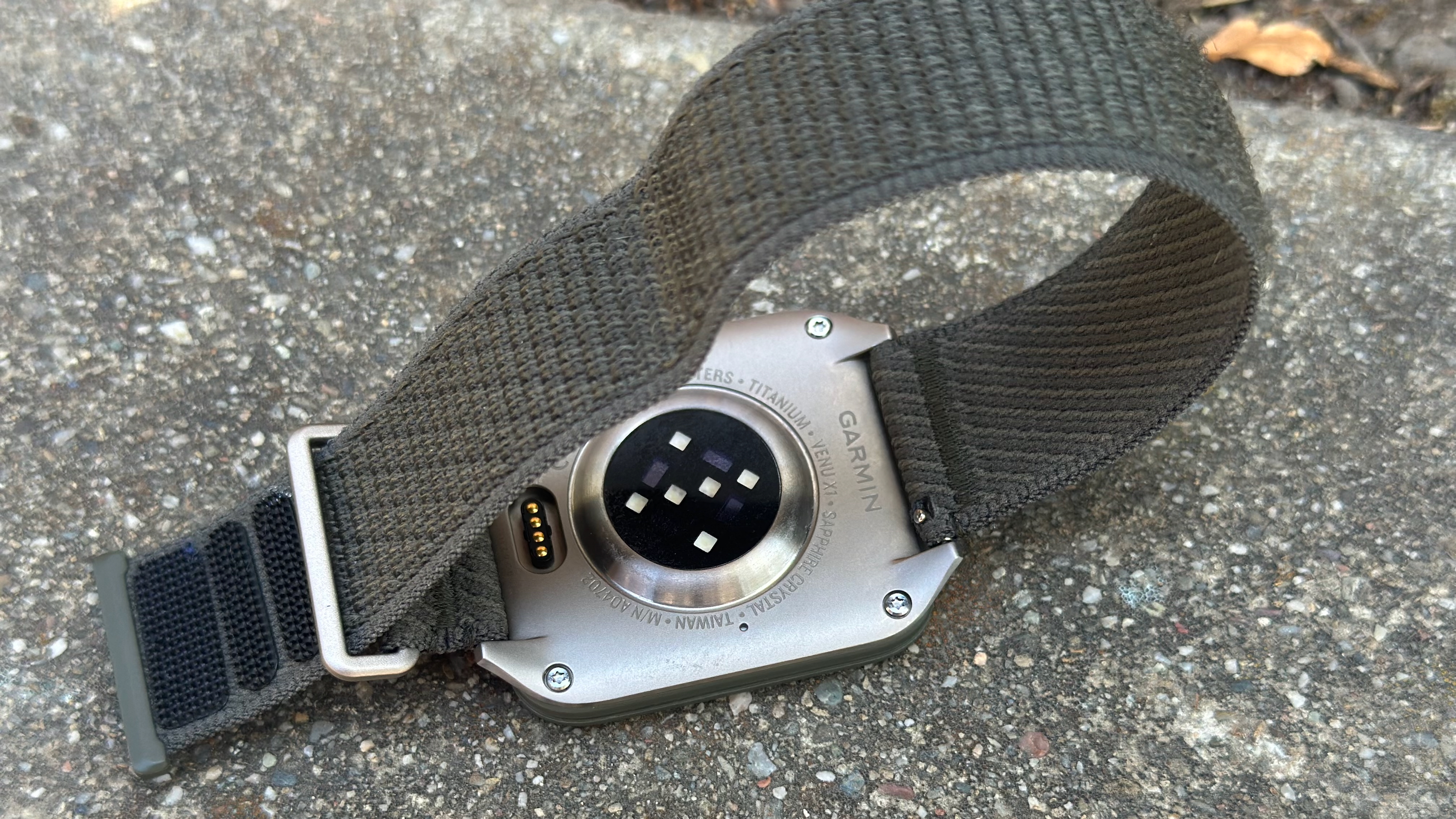 The Garmin Venu X1 sitting upside-down on asphault, with the words 