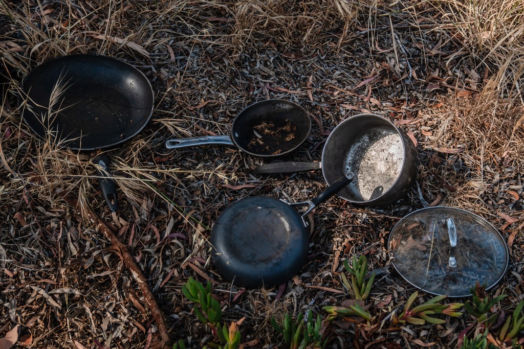 Pots and pans can be seen on the ground at a homeless encampment next to state Route 94 East freeway in Golden HIll on July 15, 2025. / Ariana Drehsler for Voice of San Diego