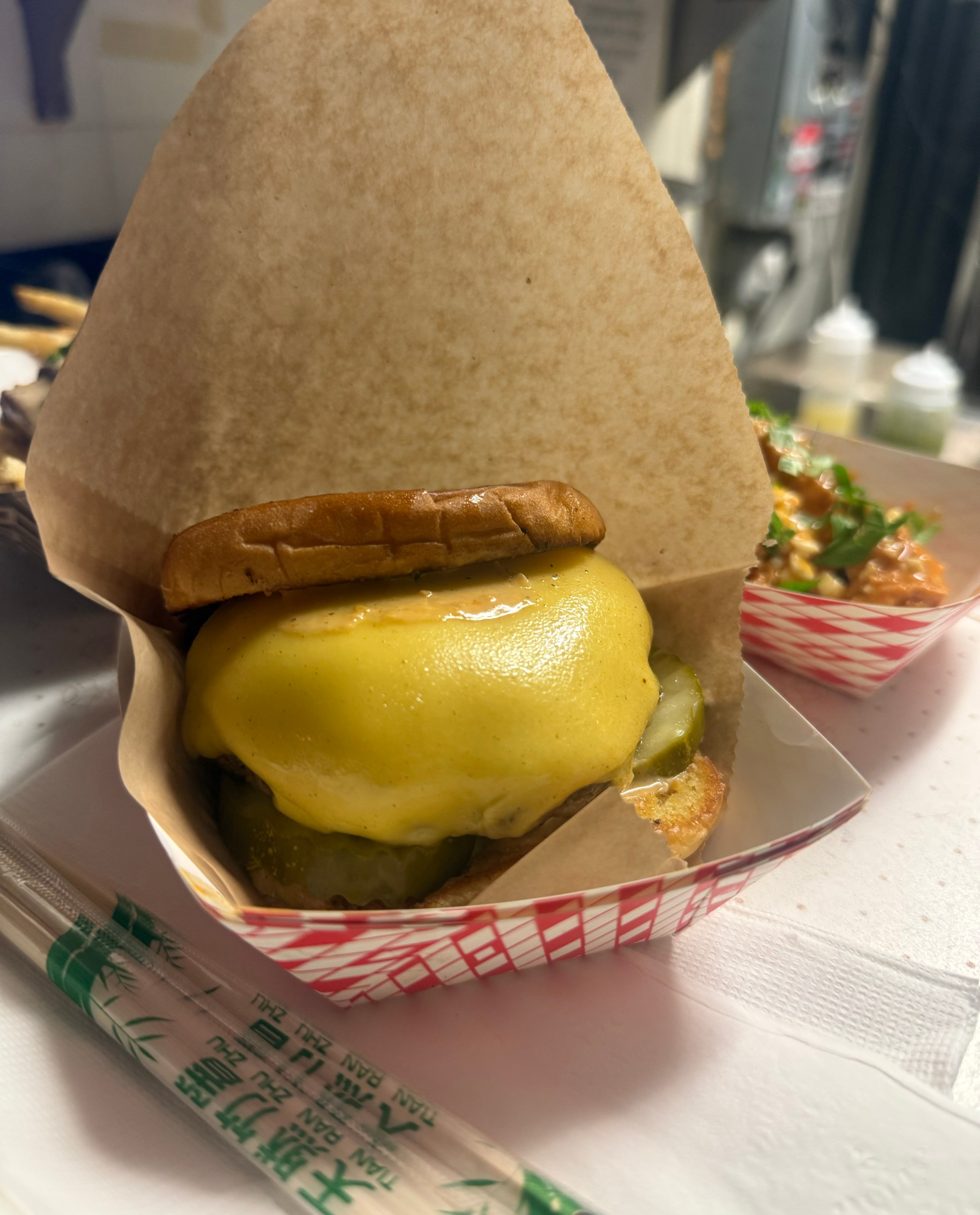 A cheese burger in a wax paper on a cardboard tray.