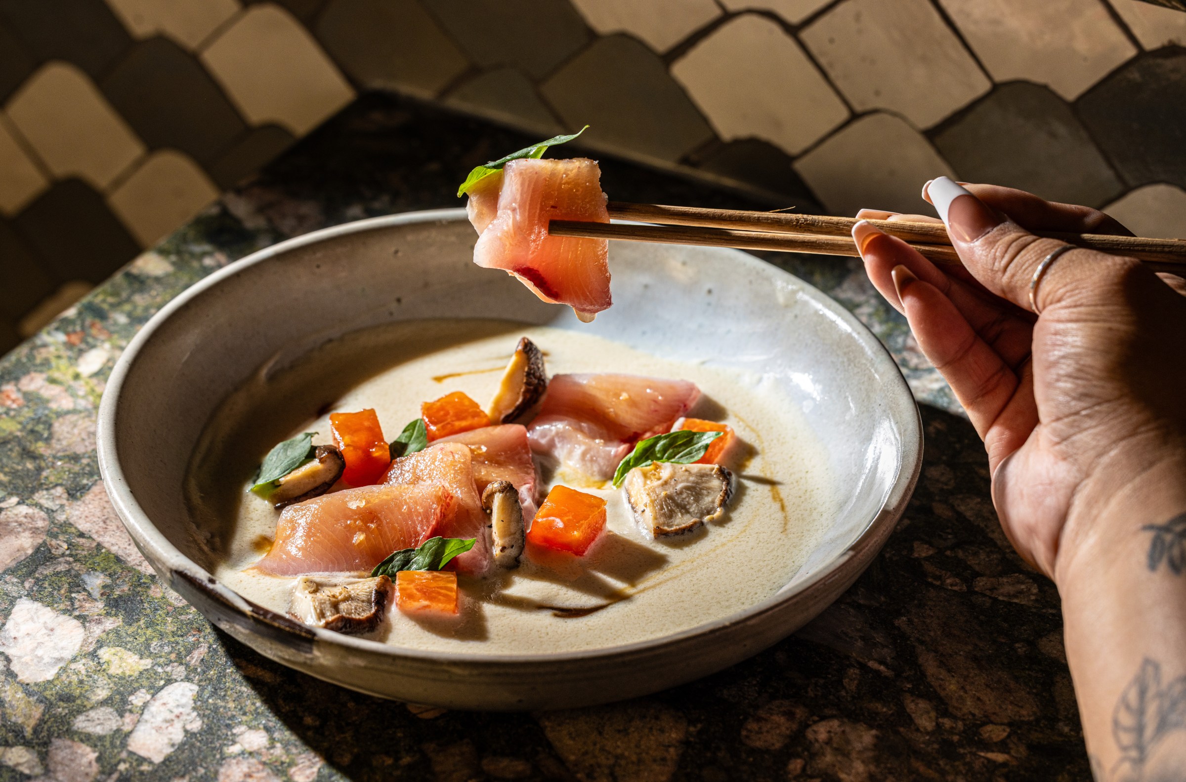 A piece of hamachi crudo is picked up with chopsticks.