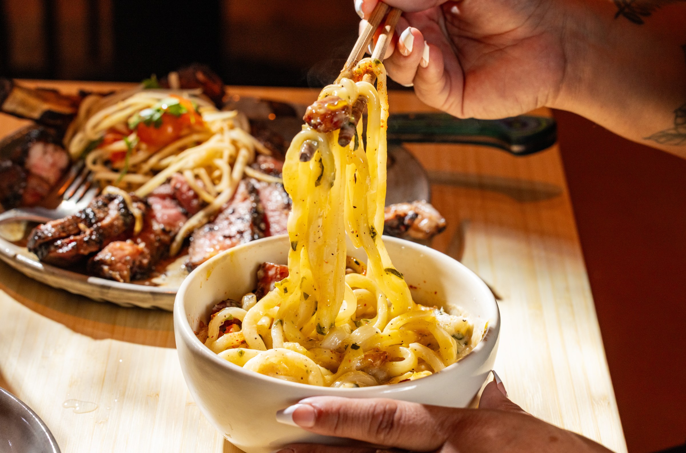 A hand pulls noodles up from a pasta dish.