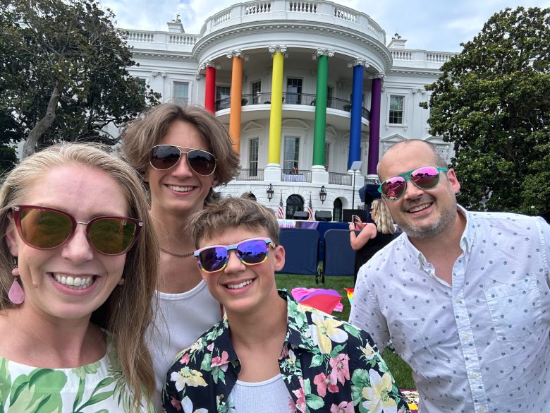 A family of four stands in front of the White House, which columns are rainbow for a LGBTQ+ pride event.