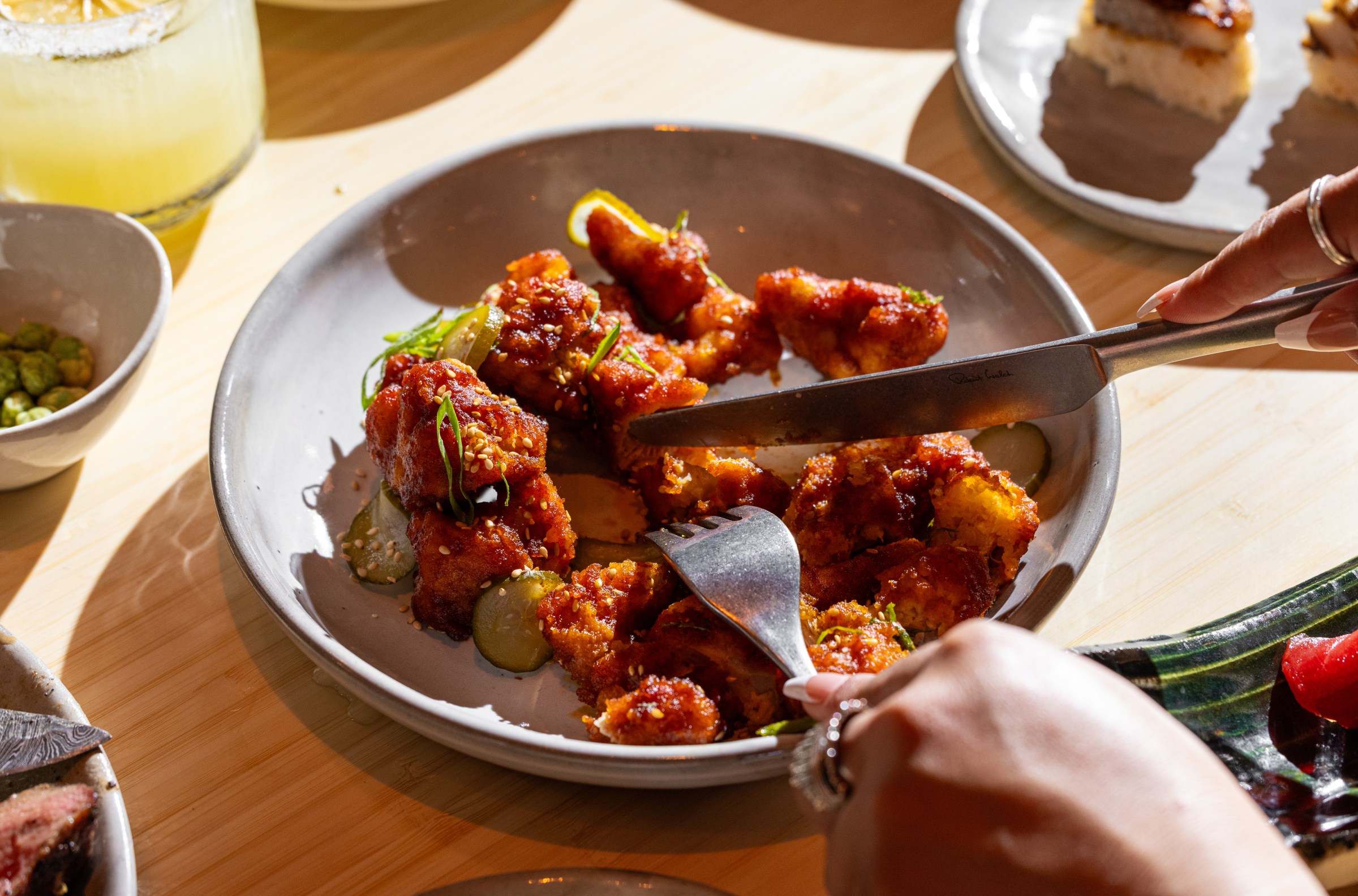 Cutting into Korean fried chicken with a fork and knife.