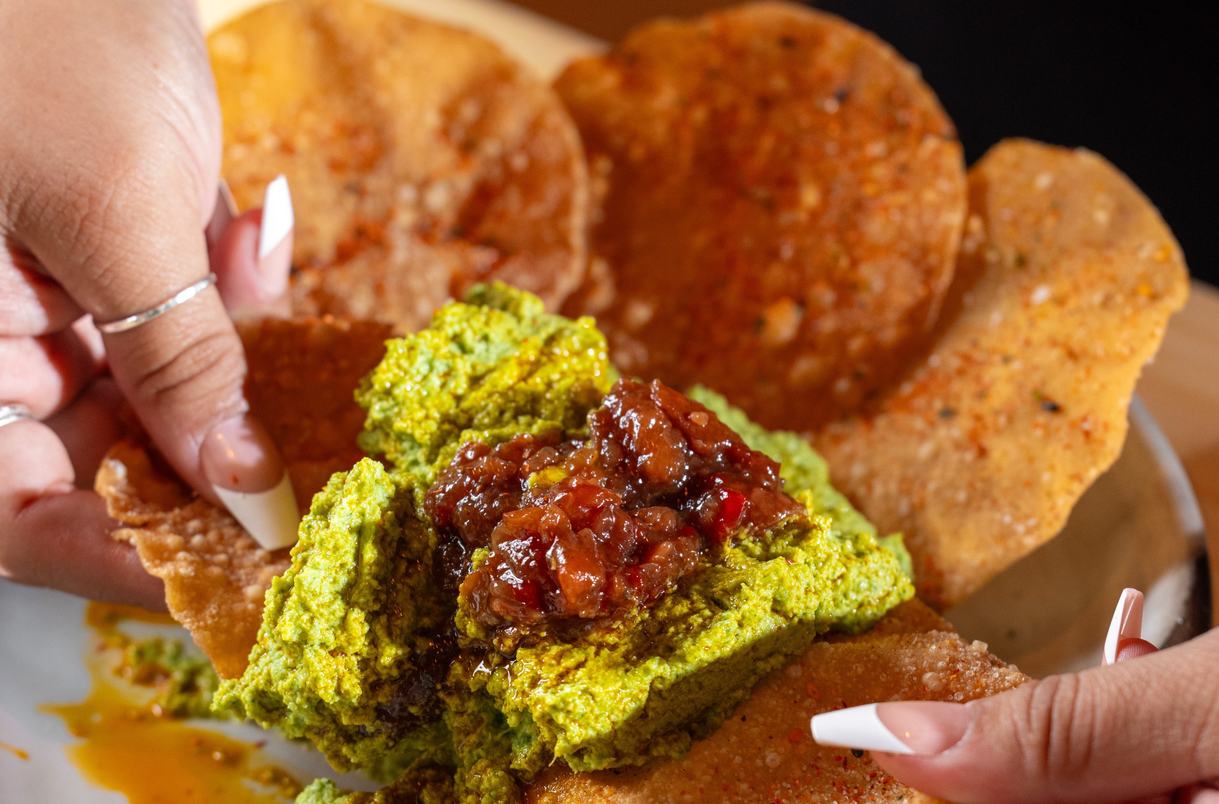 Hands break up a wonton chip holding edamame hummus.