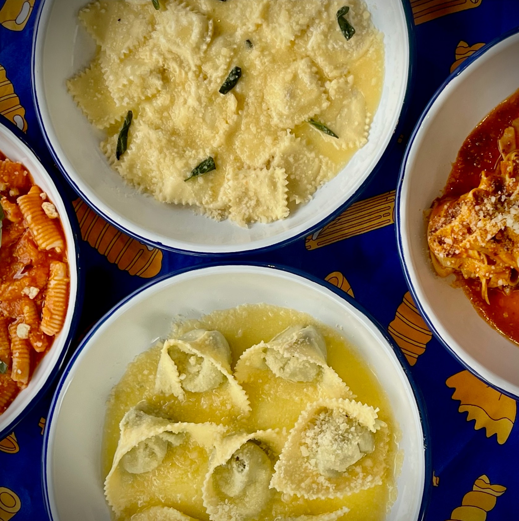 A table with four pastas, two in cream colored sauce, and the other two in red sauces.