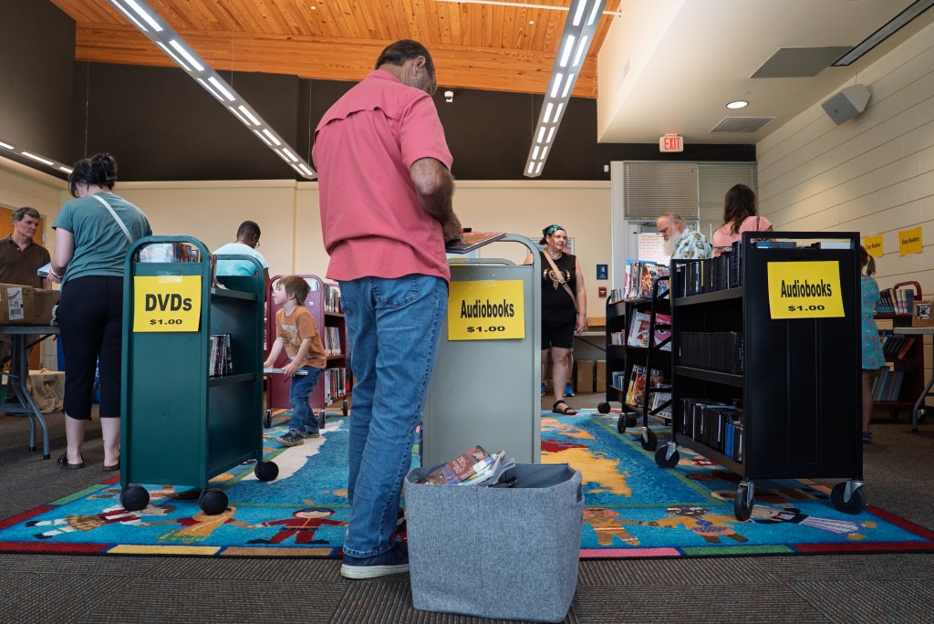 A person wearing a red shirt and blue jeans browses through rows of books during a sale.