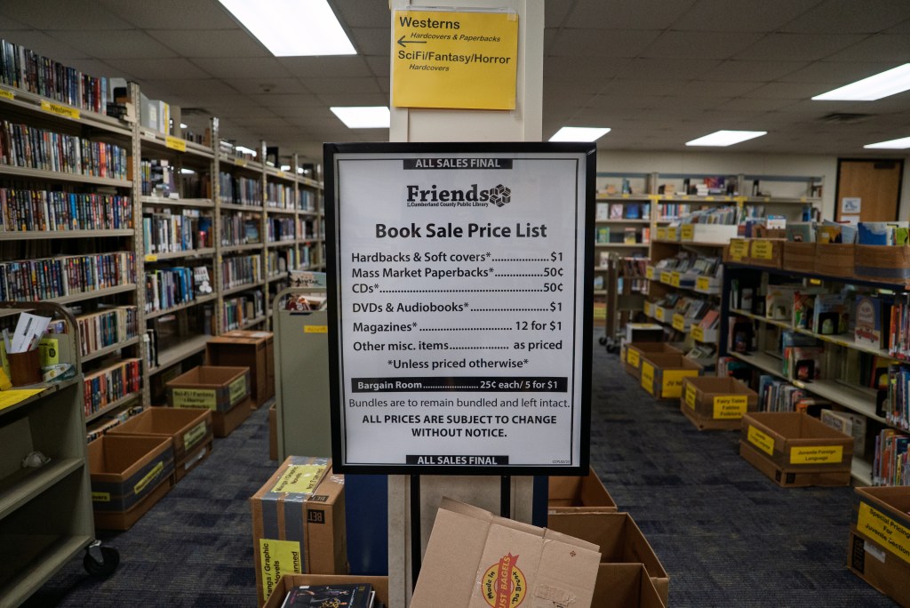 A column in a library displays the prices of the Friends of the Cumberland County Public Library Book Sale, breaking down the prices of hardbacks and soft covers, CDs, DVDs and audiobooks, and more.