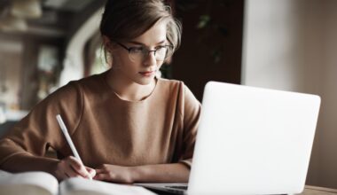 A person is sitting in front of her open PC and writing on a paper.