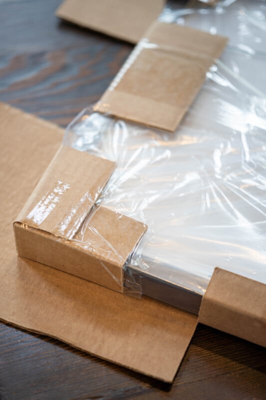 A close-up of a cardboard package partially opened, revealing a plastic-wrapped item inside, placed on a dark wooden surface.