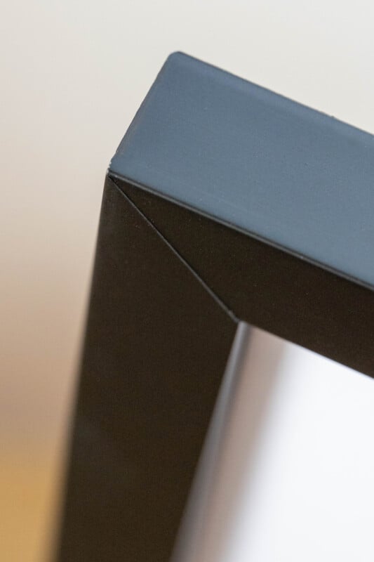 Close-up of the top corner of a black picture frame with a white background, showing the sharp edges and smooth surface of the frame.