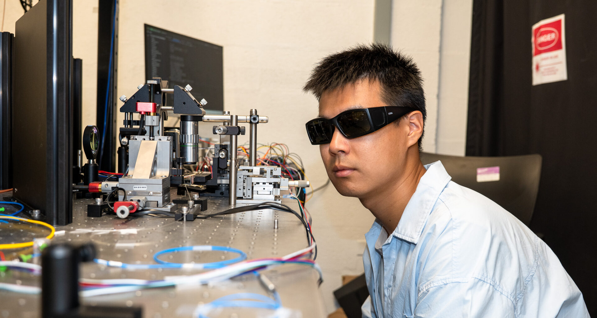 A scientist wearing goggles looks at a wire.