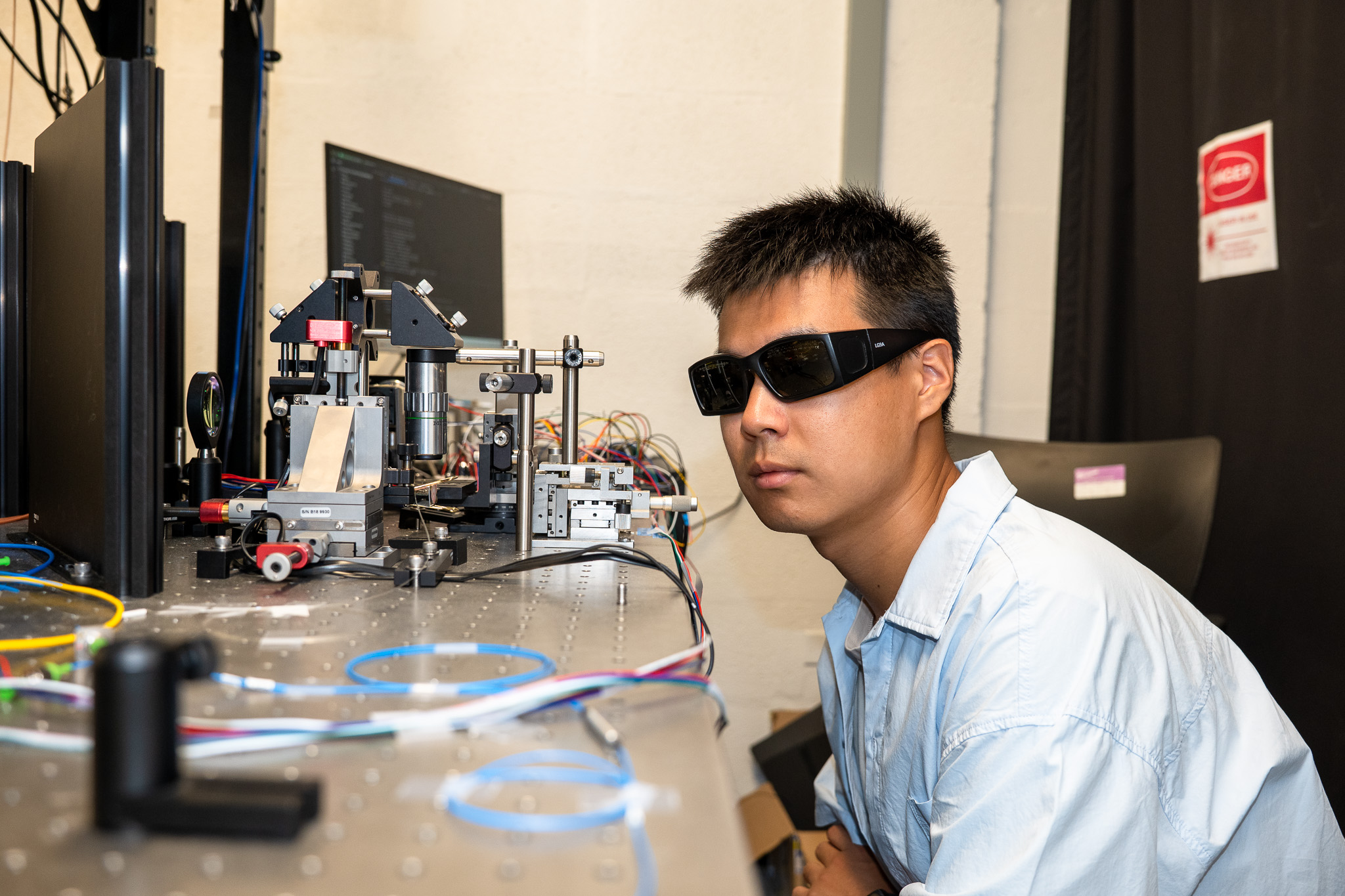 A scientist wearing goggles looks at a wire. 