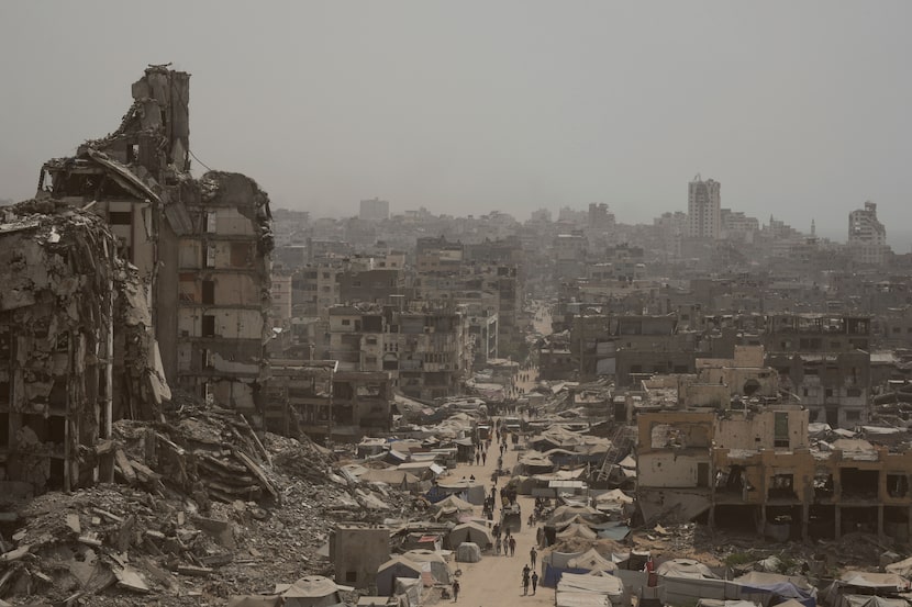 People walk down a street surrounded by buildings destroyed by Israeli bombardments in the...