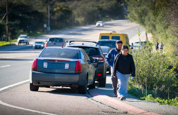 Hikers walk next to parked vehicles on the shoulder of state Route 67 near Mt. Woodson, on the way to the trail head to Potato Chip Rock. Four new parking areas are designed to provide safer parking on the west side of SR-67 south of Archie Moore Road.(Howard Lipin / For The San Diego Union-Tribune)