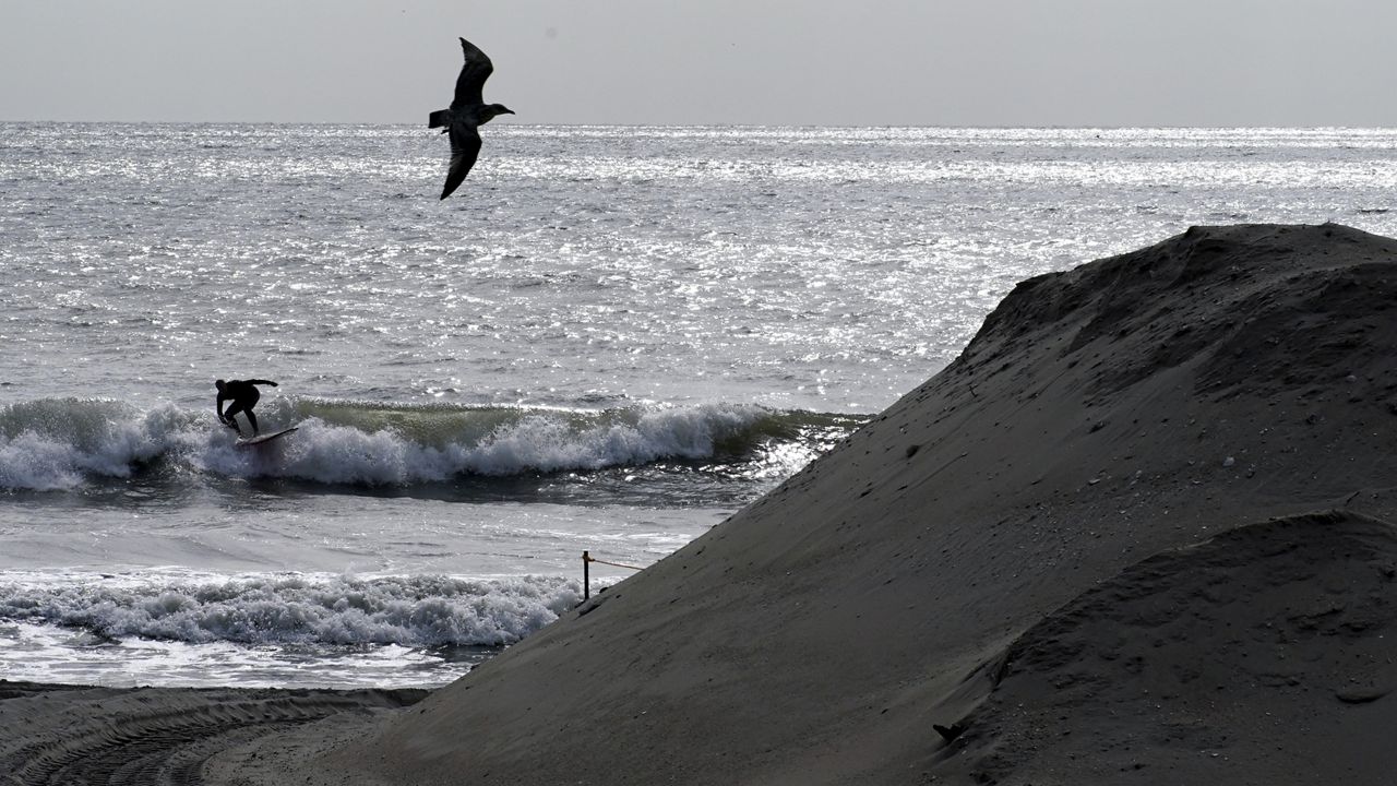 A person surfs by an artificial sand dune, Tuesday, Oct. 18, 2022, in the Far Rockaway neighborhood of the Queens borough of New York. While some parts of Rockaway Beach are currently closed due to the U.S. Army Corps of Engineers' Atlantic Shorefront Resiliency Project, others continue to be popular with surfers and other beachgoers. (AP Photo/Julia Nikhinson)