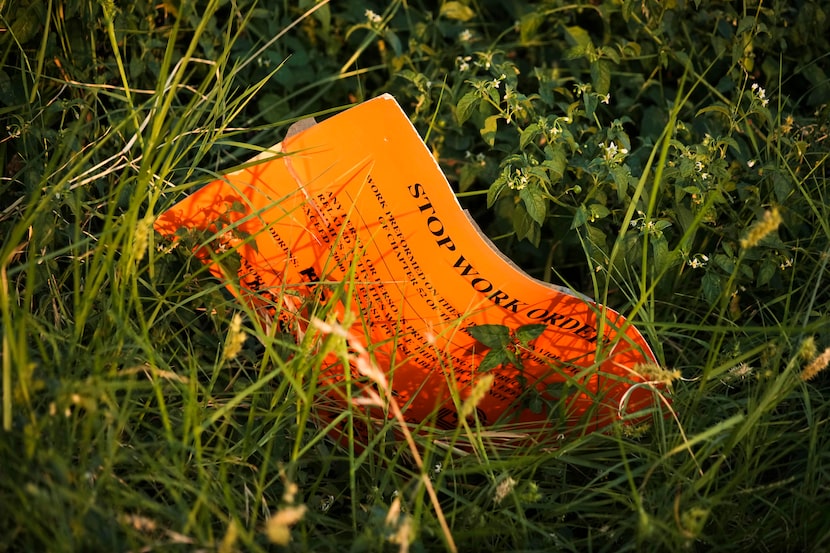 A City of Dallas stop work order for the property  is seen in a patch of weeds next to a...