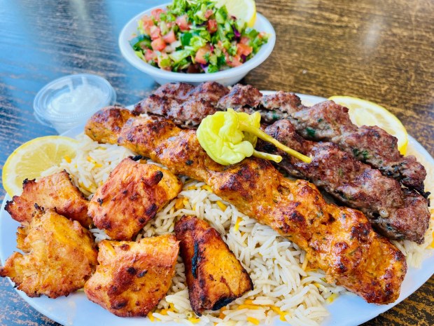 The mixed grill plate at Mal Al Sham with two beef kabobs skewers, one chicken kabob skewer and one chicken tikka skewer with a side of rice and salad. (Carlos Rico / The San Diego Union-Tribune)