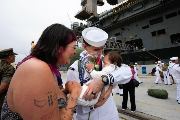 Kaleb Enrriques leans in to kiss his 10-month-old son, Aralias, as his wife, Mia Enrriques, looks on. Enrriques was among the sailors onboard the USS Carl Vinson who returned from deployment to their homeport at Naval Air Station North Island on Thursday, Aug. 14, 2025, in Coronado, CA.  (Nelvin C. Cepeda / The San Diego Union-Tribune)
