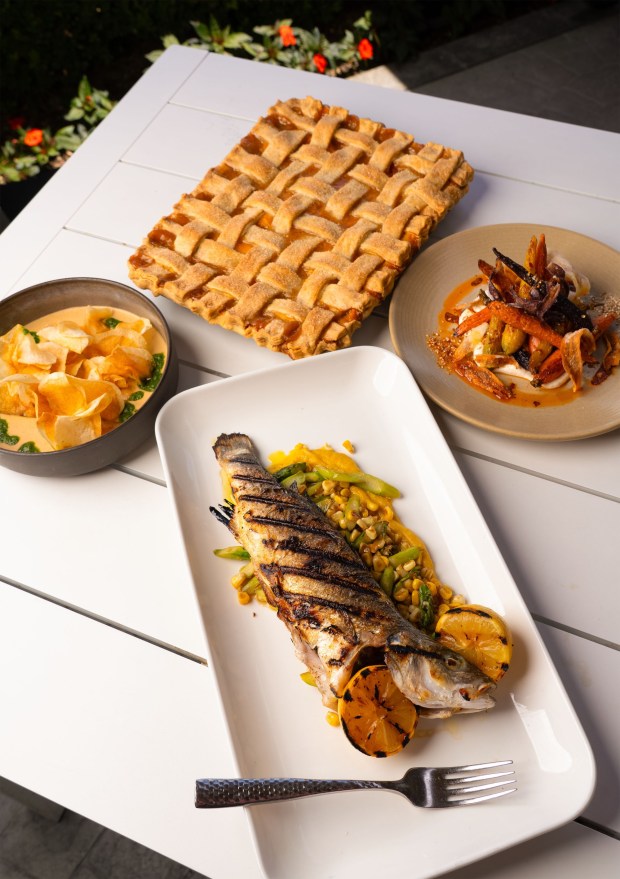 Emily Brubaker, resort executive chef at Omni La Costa in Carlsbad, prepared, from foreground center, grilled branzino with pan roasted corn, asparagus and corn puree, upper left, anchovy and white bean dip with potato chips, top center, bourdon brown sugar peach slab pie, and upper right, roast carrot salad with orange coriander labneh and harissa vinaigrette's, at the Vue, one of eight restraints she oversees at the resort. She won season 1 of the NBC culinary competition show, " Yes, Chef!" hosted by Martha Stewart and chef Jose Andres to take home the $250,000 prize. Photographed Thursday July 24, 2025, in Carlsbad, California. Howard Lipin / For The San Diego Union-Tribune)