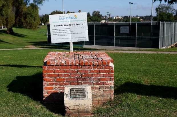The crumbling brick pedestal where the sculpture once stood is seen along with a sign detailing new sports courts at Mountain View Community Park on Thursday, July 31, 2025. (Meg McLaughlin / The San Diego Union-Tribune)