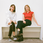 Two smiling women sit on a bench.