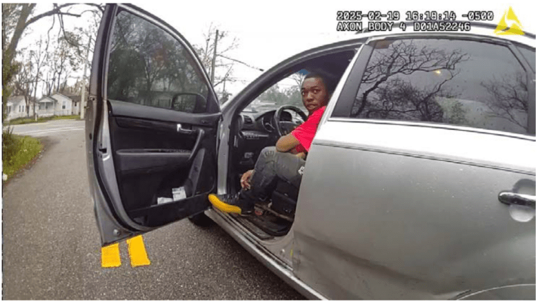 William McNeil, Jr. is seen sitting in the drivers' side of his car with the drivers' side front door open.