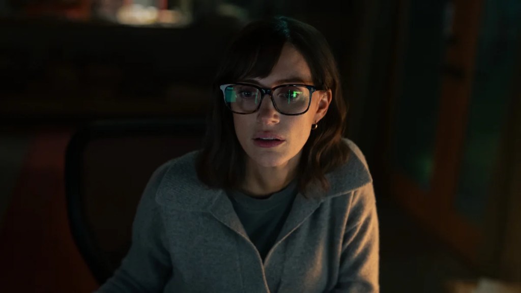 Jessica Chastain wearing glasses sits in a dark room with her face and the left side of her body partially illuminated