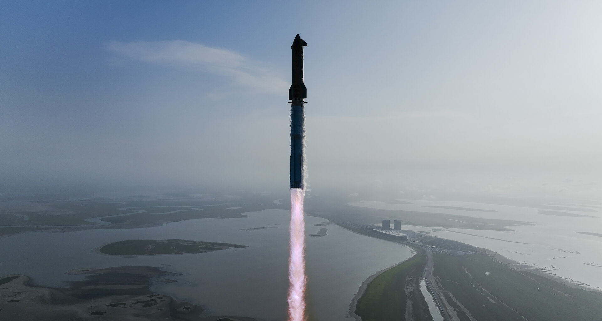 a huge silver rocket launches into a blue sky from a seaside pad