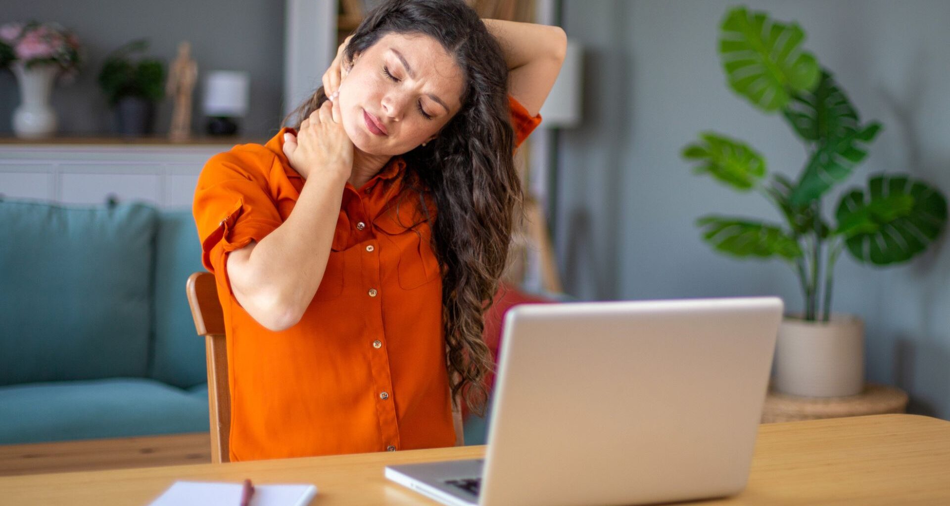 woman holds onto painful neck in front of laptop