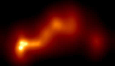 A glowing string of orange and yellow gas in the darkness of space, with a yellow end on the left showing a gas jet of a black hole