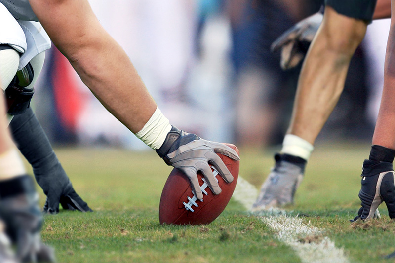 Close-up of a football player holding the ball at the line of scrimmage during a game.