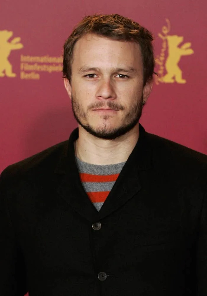 A man in a black suit jacket and striped shirt stands against a backdrop with an illustrated bear, suggesting a film festival event
