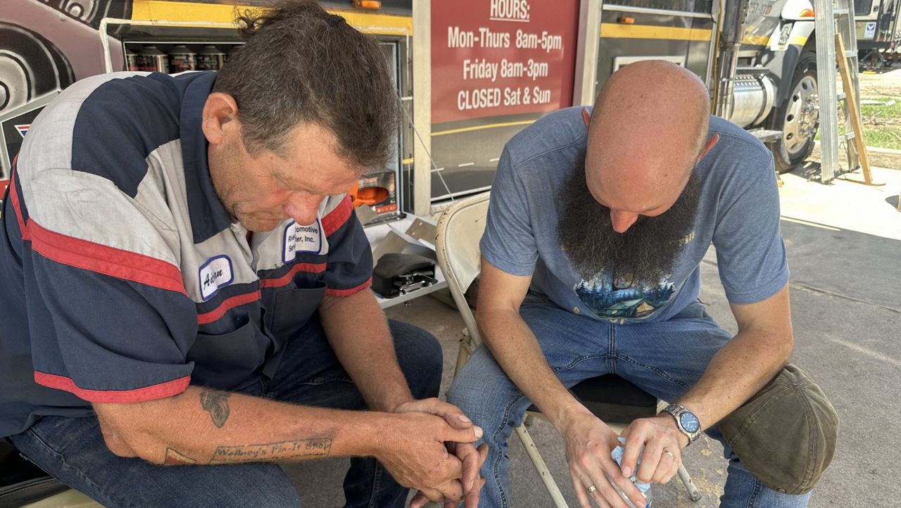 Kerrville mechanic Adrian Wollney prays with a recovery worker in Hunt, Texas. (Spectrum News 1/Bryan Boes)