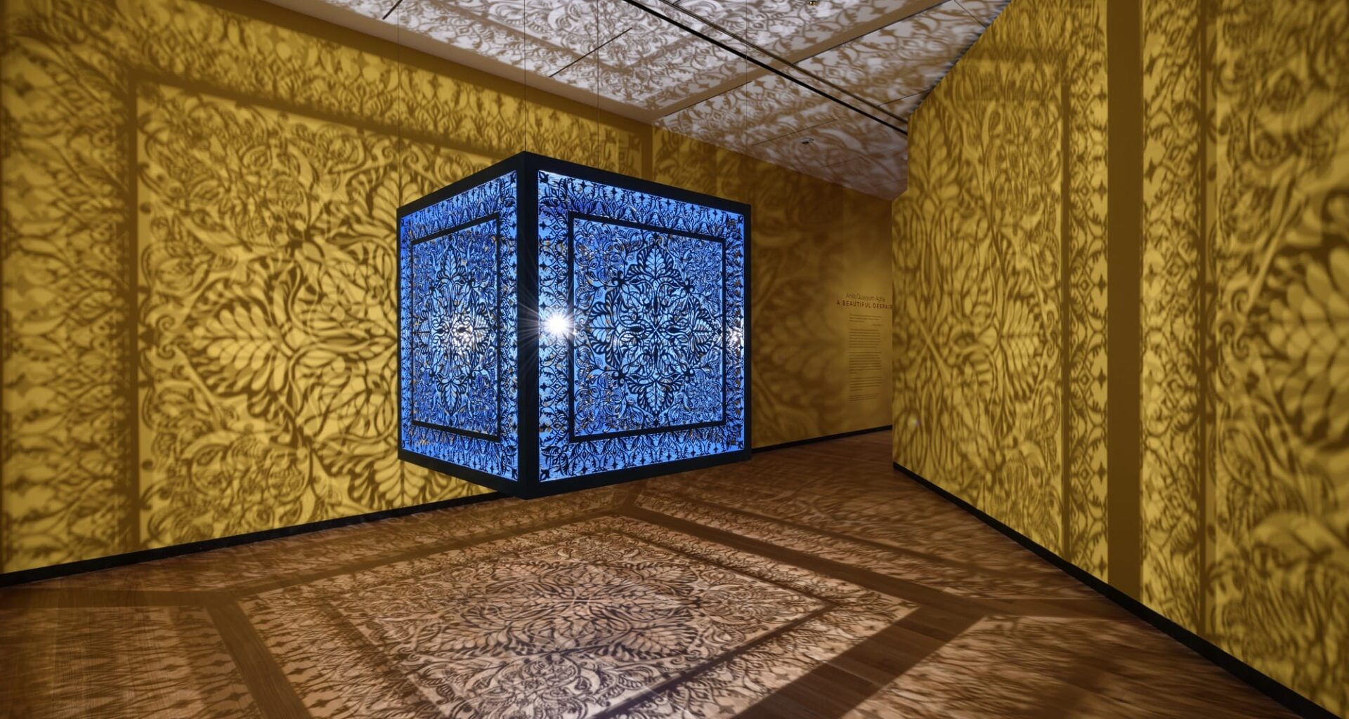 a sculptural installation in a yellow room, with light emitting from within a structure that casts ornate shadows onto the walls