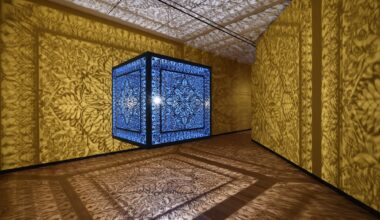 a sculptural installation in a yellow room, with light emitting from within a structure that casts ornate shadows onto the walls