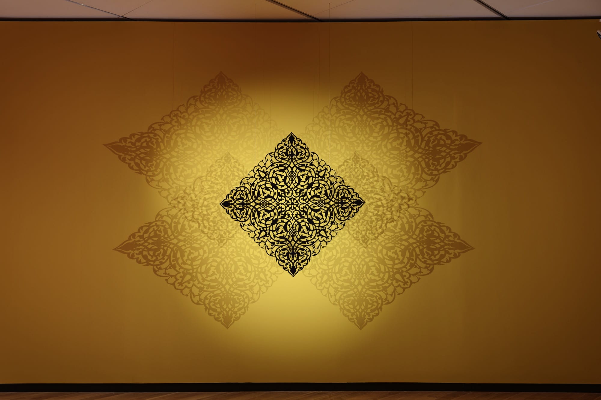 an elaborate cut-out set against a yellow wall, with light shining through to cast ornate shadows onto the wall
