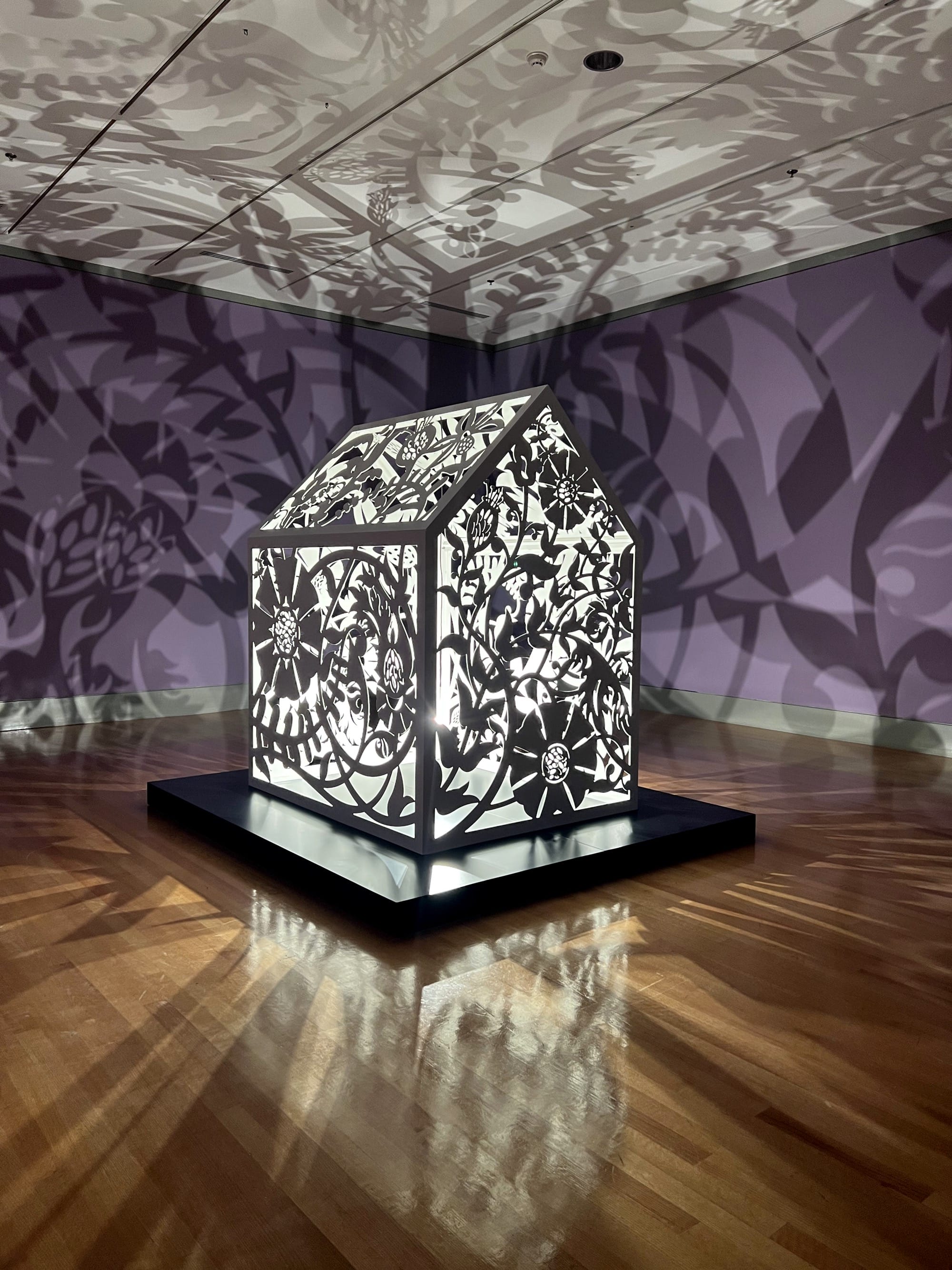 a sculptural installation in a violet room, with light emitting from within a structure that casts ornate shadows onto the walls