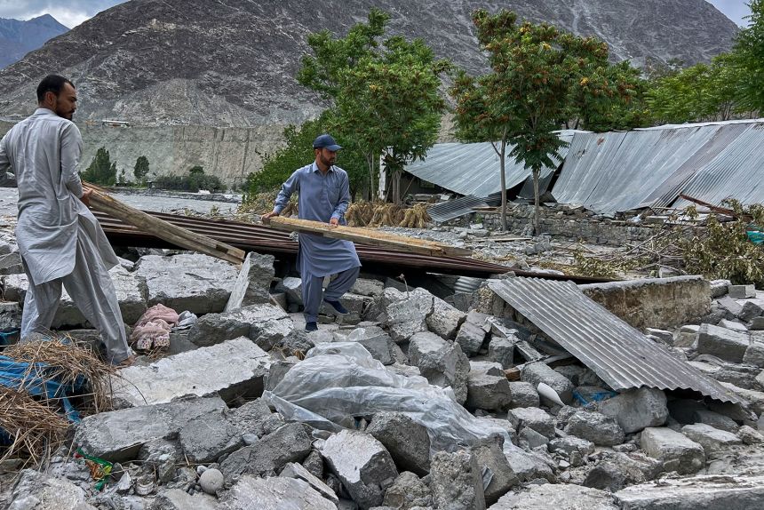 Saqib Hassan, center, and his cousin collect useful items in the rubble of their houses, which were damaged by July 22 floods, at the bank of Hunza River in Sarwarabad, a town in the northern Pakistan, on August 6, 2025.